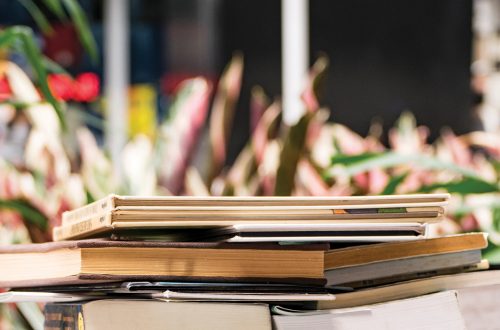 A stack of books with plants in the background.