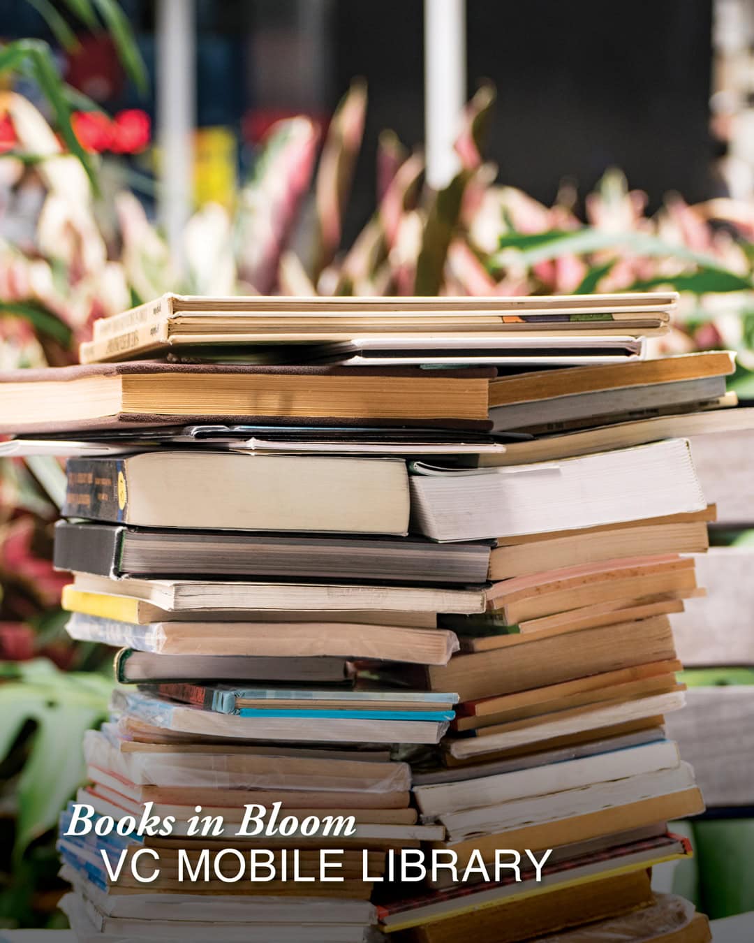 A stack of books with plants in the background.
