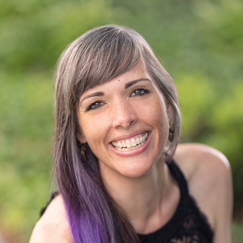 A smiling woman with purple-tinted hair enjoying summer at Ventura Botanical Gardens.
