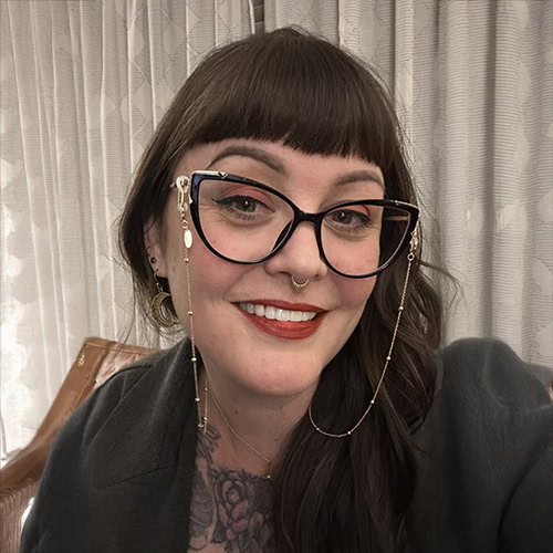 A smiling woman with dark hair, glasses, and jewelry at Ventura Botanical Gardens during Summer Humm.