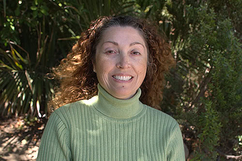 A woman smiling outdoors among lush greenery at Ventura Botanical Gardens, leadership theme.